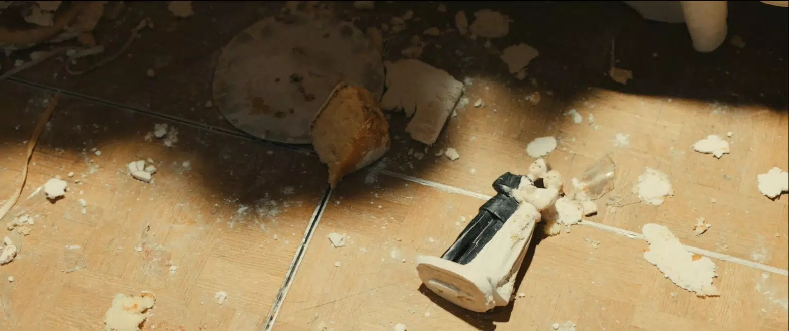 A wedding cake topper on the ground next to spilled cake