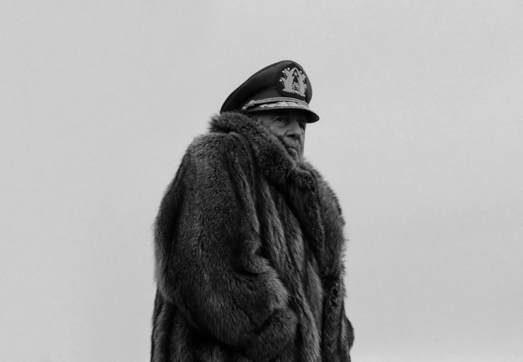 A black and white Pinochet wearing a military hat and a fur coat.