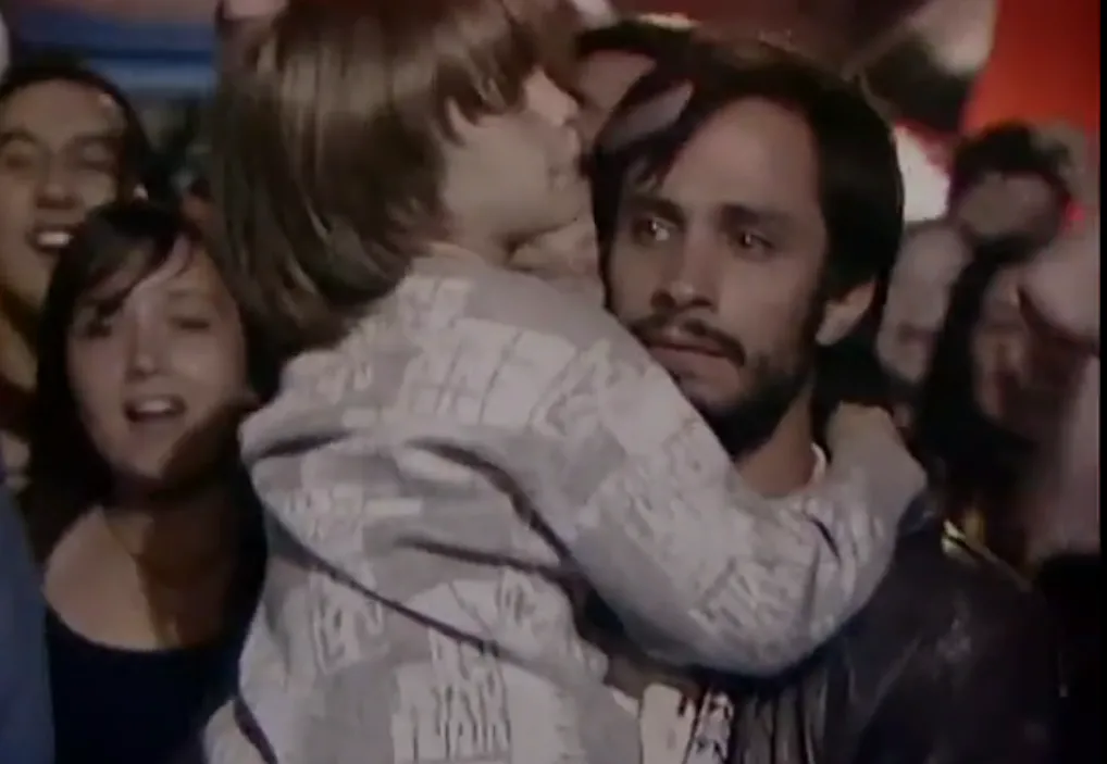 René carrying his child through a celebrating crowd.