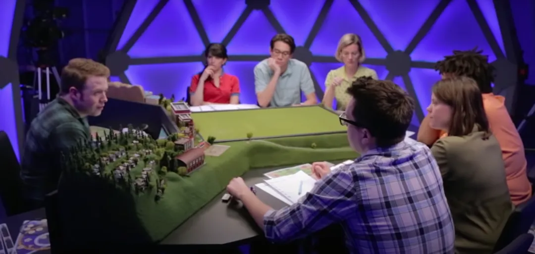 Six players sitting around a table with the Dungeon Master at its head.