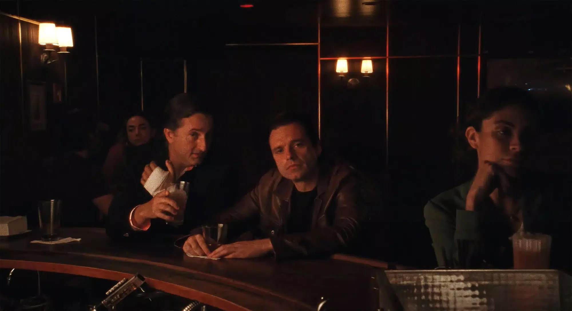 Sebastian Stan as Edward in A Different Man. He gazes across the bar. A man talks in his ear.