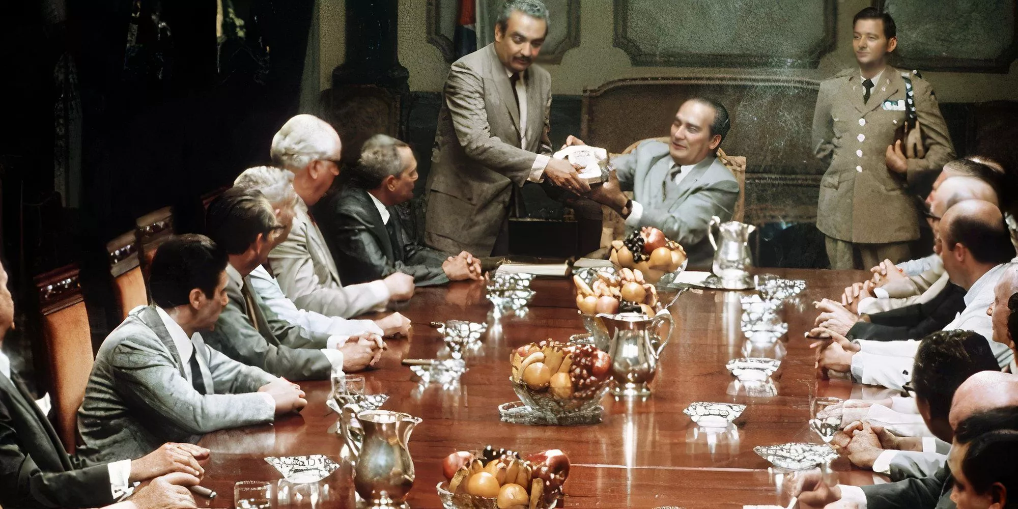 Al Pacino and Lee Strasberg sitting at a long table with several other men in The Godfather: Part II (1974)