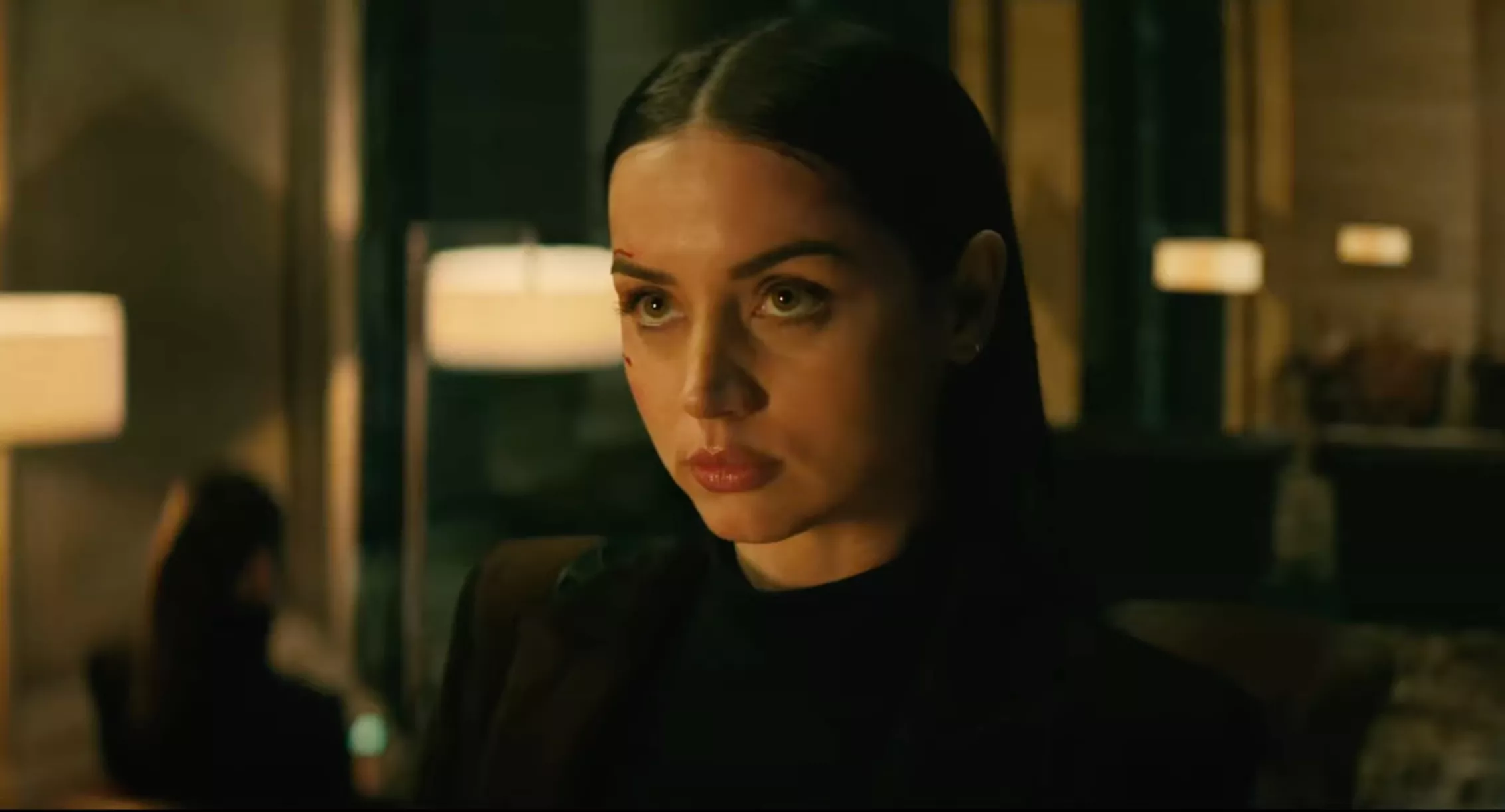 a woman in black with a cut on her face stares menacingly